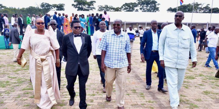 DP President Norbert Mao (in black suit), walks to the podium at his homecoming in Gulu City, escorted by (L-R): Ms Lydia Wanyoto of NRM Women's League, NRM deputy supremo Al-hajj Moses Kigongo, and President Museveni's brother, Gen Salim Saleh.